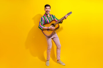 Full body photo of young excited man in retro garment playing on acoustic guitar touching strings...