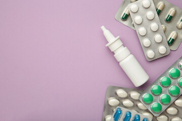 Nasal spray with pills on purple background. Top view