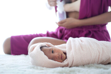 Fototapeta na wymiar Newborn baby wrapped in a cloth lies on a bed while the mother pumps milk using a manual breast pump in a blurred background