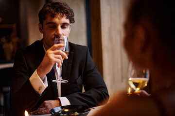 handsome man drinking white wine near girlfriend during date on Valentines day, romantic dinner
