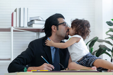 Cute little girl shows her love by kissing her father on the desk at father's office