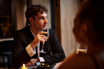 handsome man holding glass of wine near girlfriend during date on Valentines day, romantic dinner