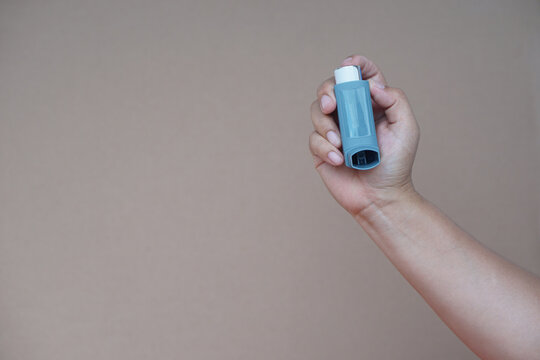 Close up woman hand hold asthma inhaler, brown background. Concept, health care. Pharmaceutical products for treatment symptoms of asthma or COPD. Use under prescription. Health care device at home.  