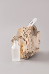 A transparent matte cosmetic bottle and a pipette filled with a natural remedy lies on a large textured stone. Cosmetics of nature. Natural care.