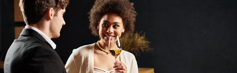 african american woman holding wine glass and looking at man during date on valentines day, banner