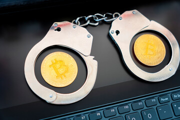 golden bitcoin on the background of handcuffs and a black laptop keyboard. Prohibition of the sale...