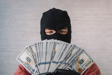 the concept of crime and money theft. Male thief with balaclava on his head holding a handful of...
