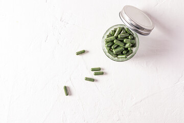 Open glass jar with lid filled with organic spirulina capsules on white background with copy space....