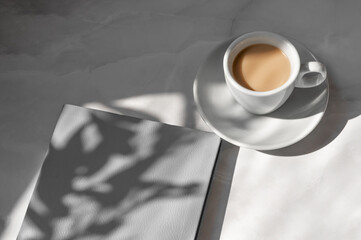 Notebook with gray textured cover, ceramic white saucer and cup with coffee drink on neutral marble...