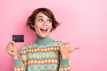 Portrait of astonished attractive lady hold debit card look indicate finger empty space isolated on...