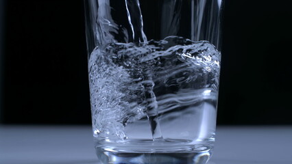 Pouring water into glass cup in super slow-motion captured with high-speed camera in black backdrop