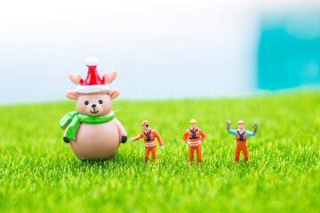 Miniature worker with Reindeer doll on green grass with space on blurred background, outdoor day light, Christmas holiday concept