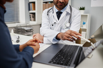 Obraz premium Cropped shot of male doctor showing information about treatment to patient using wireless laptop sitting at desk in clinic office