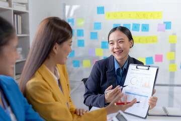 Asian businesswomen collaborate and discuss business plan during team meeting in modern office.