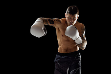 Hook. Muscular, shirtless young man, boxer training, fighting isolated over black background....