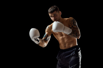 Hook. Muscular, shirtless young man, boxer training, fighting isolated over black background....