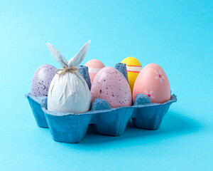 Egg wrapped in a paper in the shape of a bunny with colorful Easter eggs in carton tray. Minimal Easter concept.