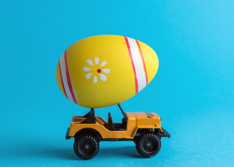 Toy car with colorful Easter egg on bright background. Minimal Easter concept.