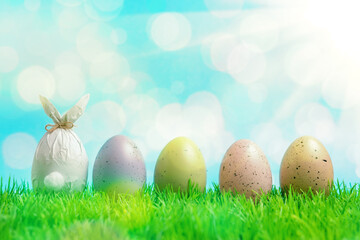 Easter egg wrapped in a paper in the shape of a bunny with colorful Easter eggs on green grass. Spring holidays concept.