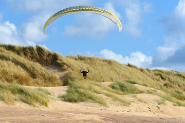 Action shot of an extreme paraglider skimming across the dunes along a beach showing amazing skill...