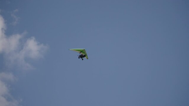 Two-seater powered hang glider flies against background of blue sky with clouds. Tourist recreational flights on ultralight aircraft in clear weather. Sightseeing private tour with pilot.