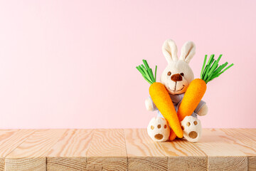 White rabbit doll with carrots on on wooden table. Minimal Easter background. Spring holidays concept.