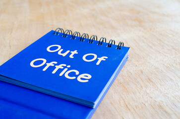 Out of office text on notepad on wooden table background. Out of office concept