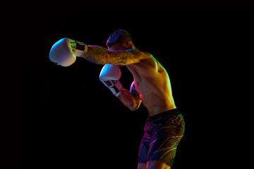 Young muscular man, boxing athlete in motion, training, fighting on ring isolated over black...
