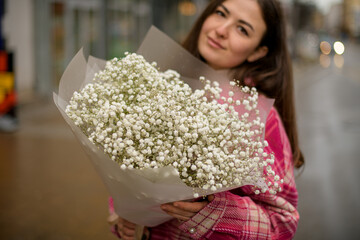 Young woman holding a bouquet of white small flowers in a transparent wrapper on a blurred background