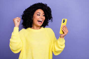 Photo portrait of lovely young lady hold telephone raise fist celebrate dressed stylish yellow garment isolated on violet color background