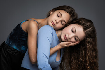 Studio portrait of two beautiful sisters with closed eyes in blue shirts against gray background
