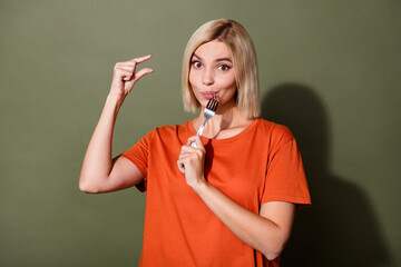Portrait of positive gorgeous girl wear orange t shirt holding small size meal low calories biting fork isolated on khaki color background