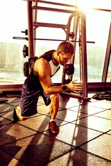 Papier Peint photo autocollant Fitness Portrait of a handsome man exercising with modern weight equipment in rays of sunlight in fitness gym.