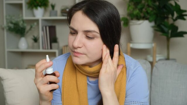A sick woman with rhinitis sprays medicine into her nose