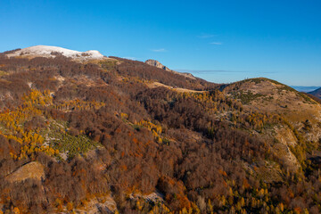 Beautiful autumn colorful view of a forest with dried leaves and the peak above covered with the first winter snow - aerial drone photo
