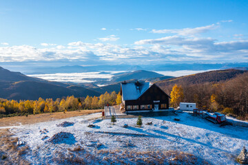 Beautiful mountain lodge on a small hill with little snow surrounded by colorful trees in autumn with a view of the valley with fog