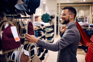 Happy man looking for a knitted hat while shopping in clothing store at mall.