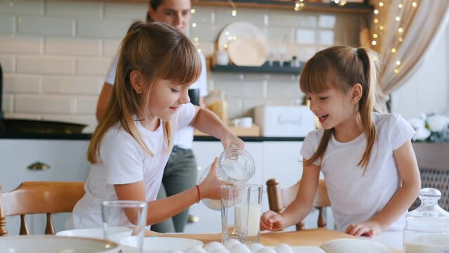 Learning how to prepare food. Mother with her little two daughters is on the kitchen with garlands.