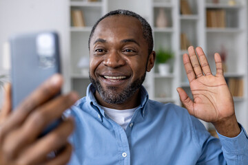 Happy smiling man using app on phone for video call, african american man smiling and looking at...