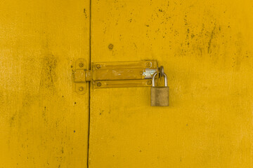 Padlock on yellow wooden gate forming a textured background.