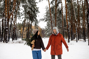 young Caucasian man and Asian woman in love walking in snowy winter forest.