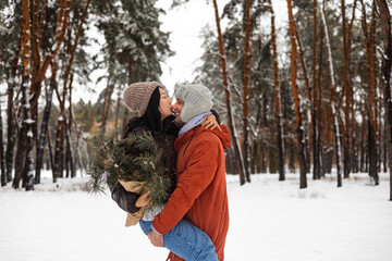 Beautiful young couple in love having fun spending winter vacation in the snowy forest, kissing and hugging in the snow.