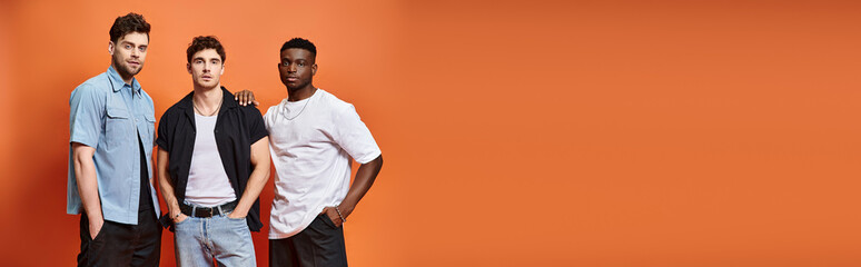 handsome diverse men in trendy urban clothes posing on orange backdrop, fashion concept, banner