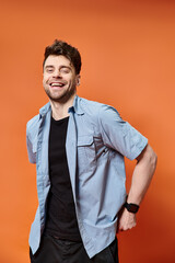 happy attractive man in casual outfit on orange backdrop looking at camera, fashion concept