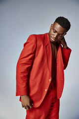 attractive african american man in vibrant red attire posing on gray backdrop, fashion concept