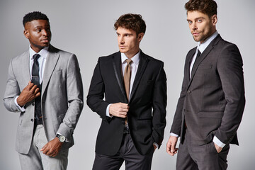 handsome stylish multicultural male models in business elegant smart suits posing on gray backdrop