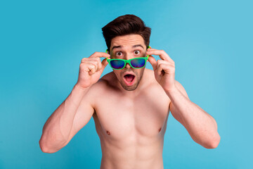 Photo portrait of handsome young guy astonished shock sunglass shirtless isolated on blue color background summer vacation