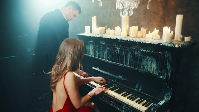 Two person fall in love Happy sexy couple play the piano together in four hands man and blonde woman enjoy romantic date. girl musician red dress bare sexy back. Guy Fashion model. dark night room. 4k