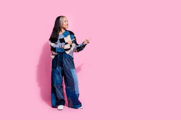 Full size photo of cute girl dressed jeans pullover oversize pants indicating look at offer empty space isolated on pink color background