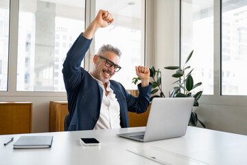 Enthusiastic mature businessman is clenching hands into fists, a happy senior business owner scream yes with triumph, having received great news of good deal, celebrating success of completed project - obrazy, fototapety, plakaty